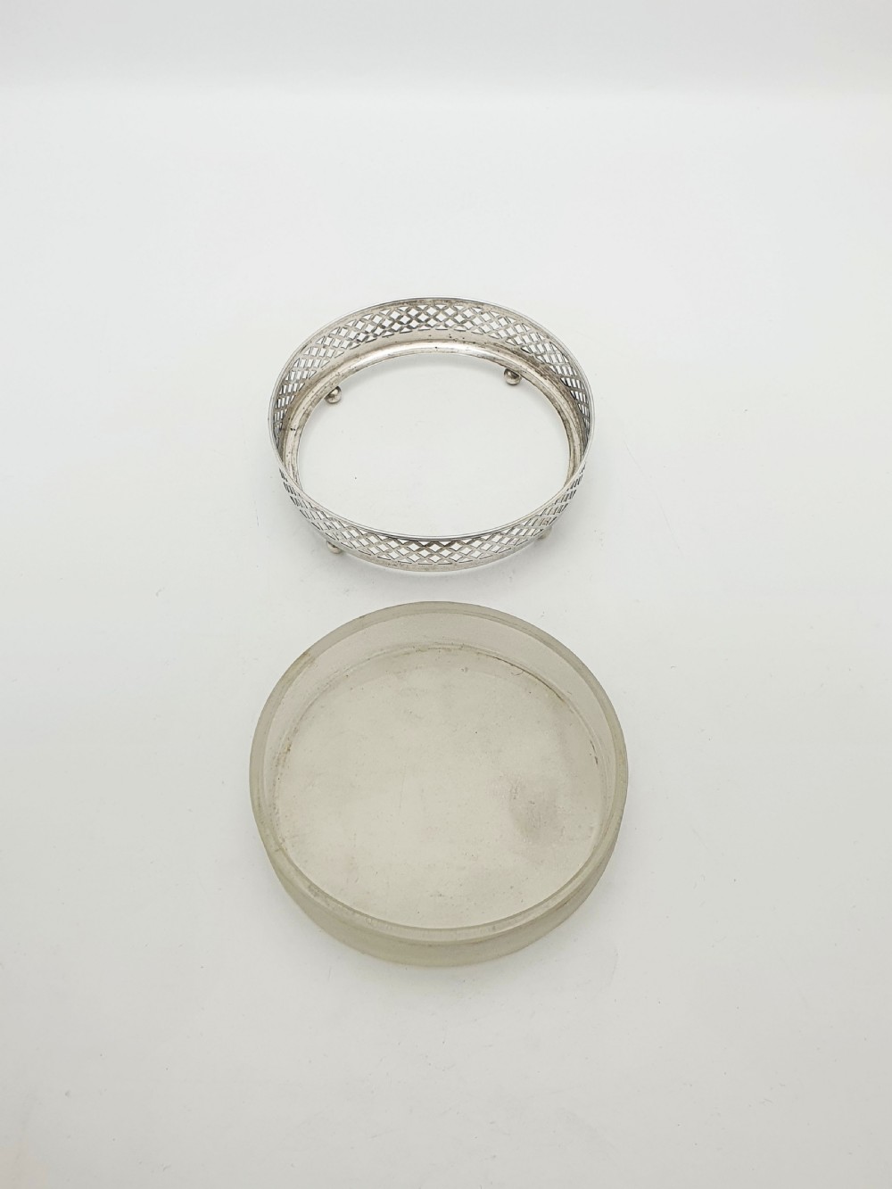A circular sterling silver dish with a pierced lattice pattern, raised on small ball feet, fitted with a clear glass insert. View II
