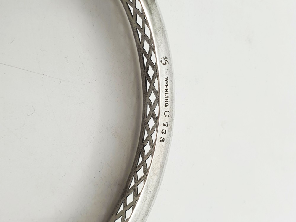 A circular sterling silver dish with a pierced lattice pattern, raised on small ball feet, fitted with a clear glass insert. View IV
