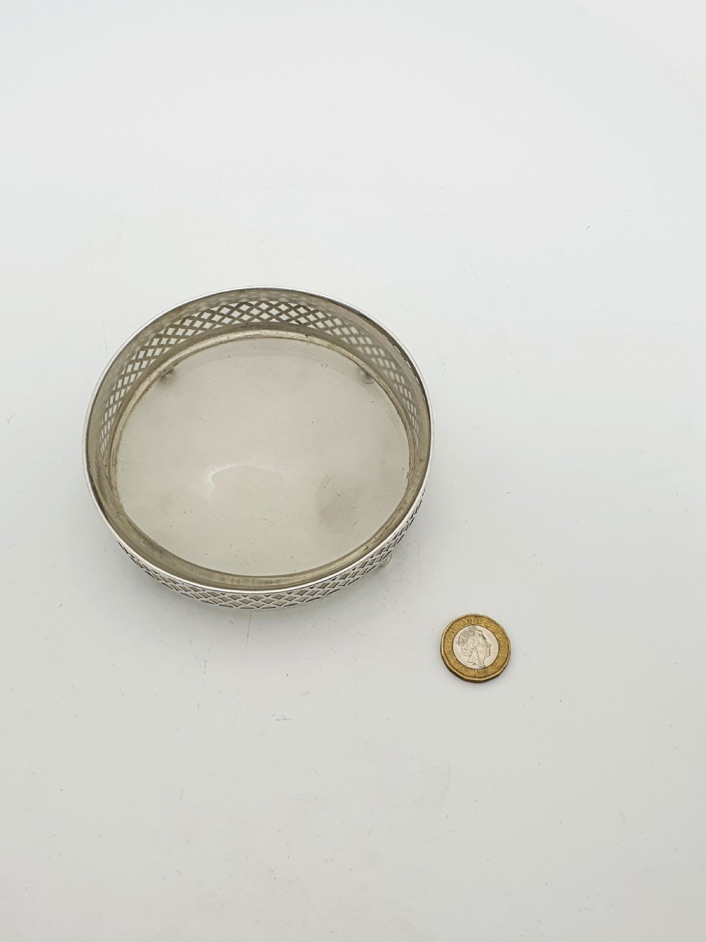 A circular sterling silver dish with a pierced lattice pattern, raised on small ball feet, fitted with a clear glass insert. View VI