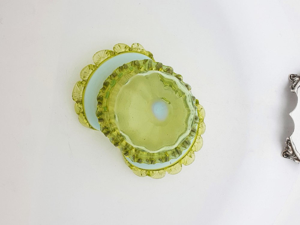 An Edwardian yellow-green vaseline glass bowl with a frilled rim set within a silver-plated frame featuring an overhead handle and ornamental feet. View IV