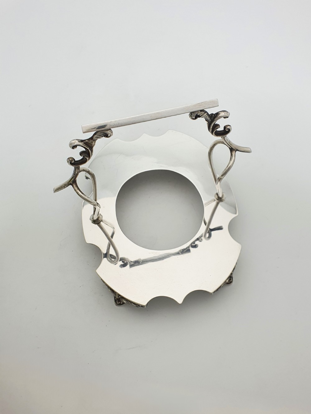 An Edwardian yellow-green vaseline glass bowl with a frilled rim set within a silver-plated frame featuring an overhead handle and ornamental feet. View V