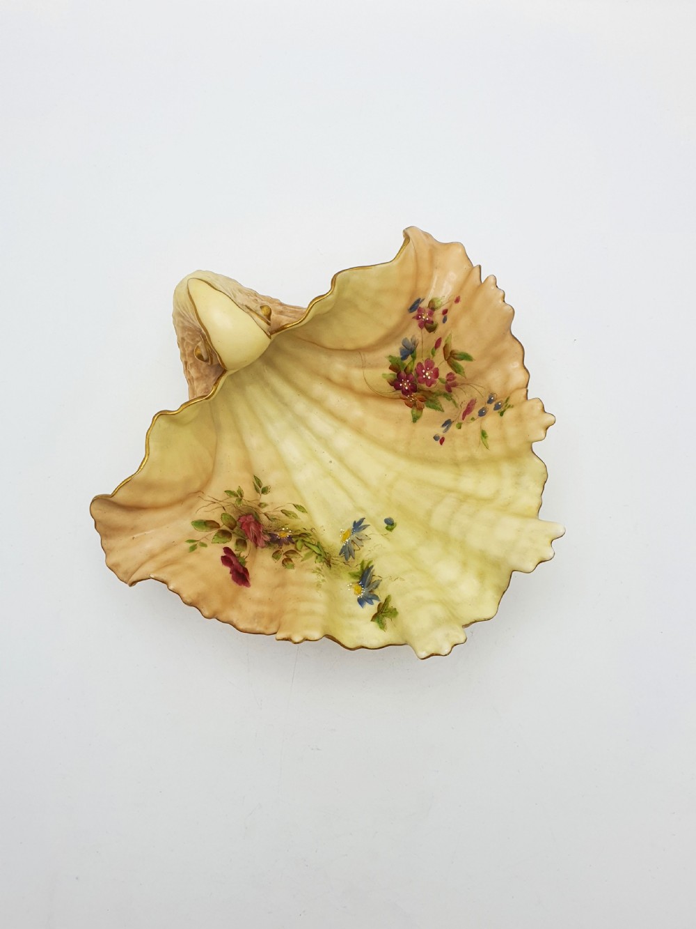 A shell-shaped antique blush ivory porcelain dish featuring soft peach shading, hand-painted pink floral sprays, textured ridges, and a gilded scalloped edge. View II