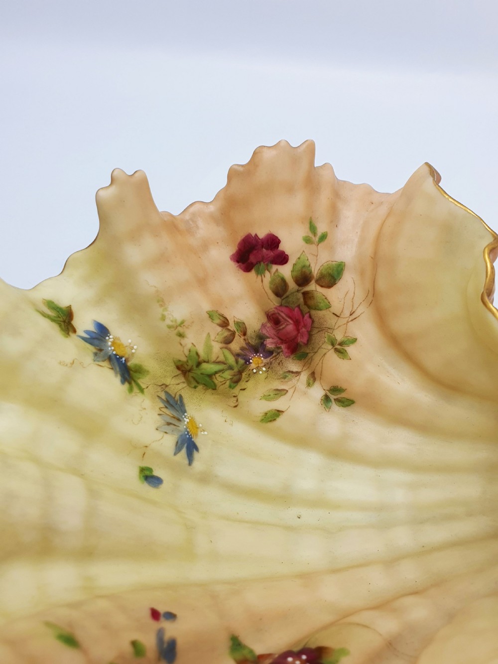 A shell-shaped antique blush ivory porcelain dish featuring soft peach shading, hand-painted pink floral sprays, textured ridges, and a gilded scalloped edge. View IV