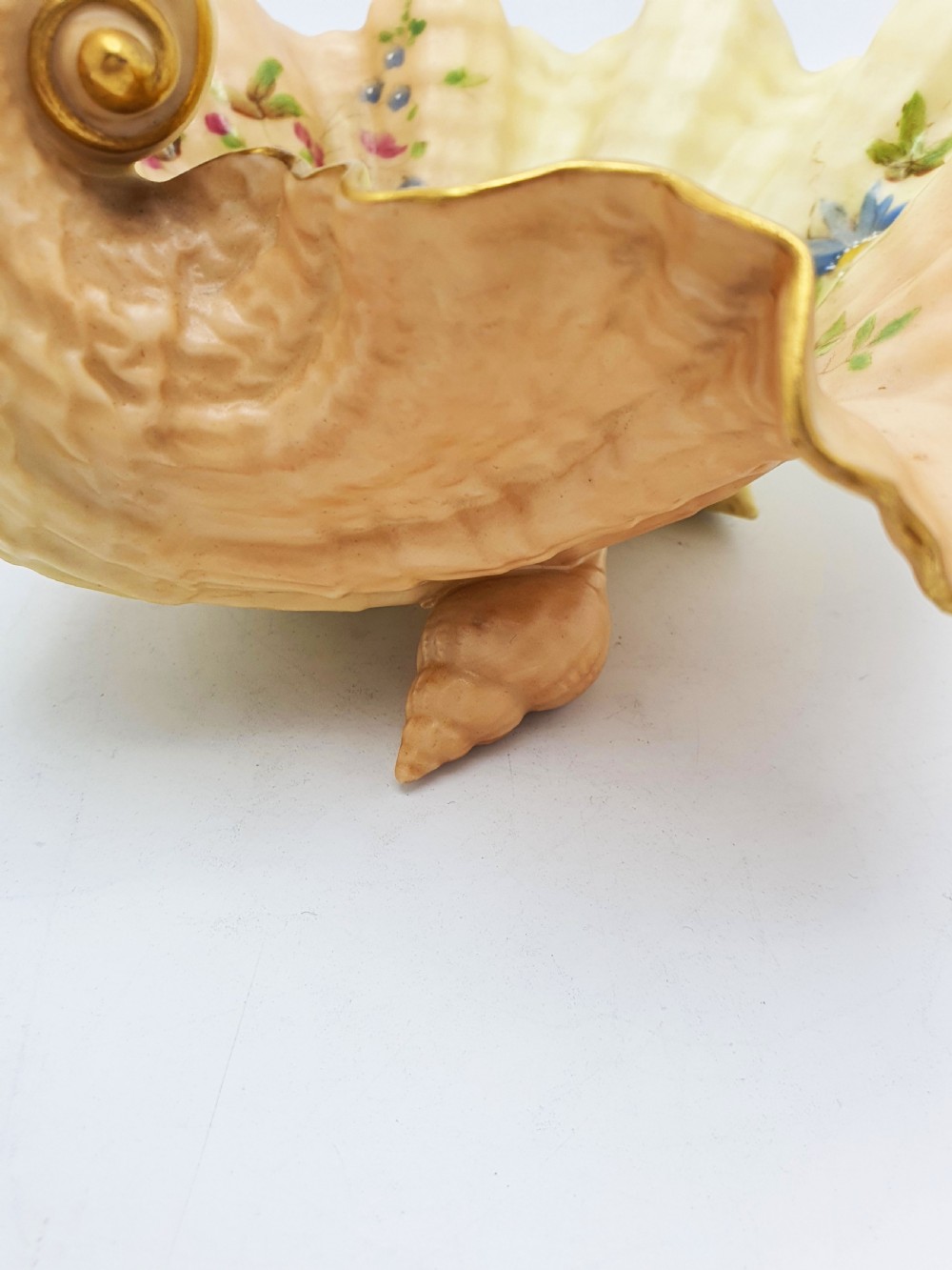 A shell-shaped antique blush ivory porcelain dish featuring soft peach shading, hand-painted pink floral sprays, textured ridges, and a gilded scalloped edge. View V
