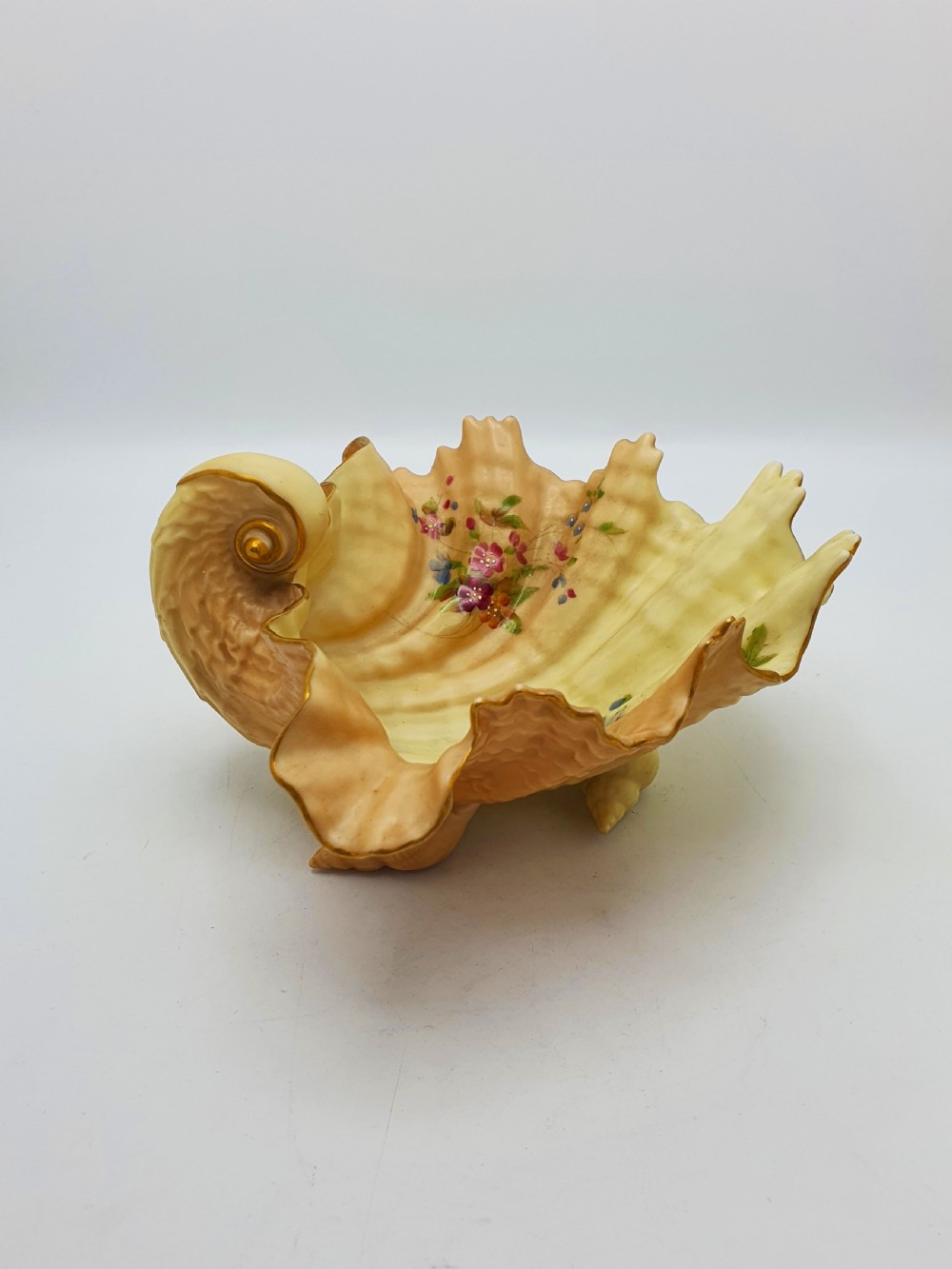 A shell-shaped antique blush ivory porcelain dish featuring soft peach shading, hand-painted pink floral sprays, textured ridges, and a gilded scalloped edge. View VI