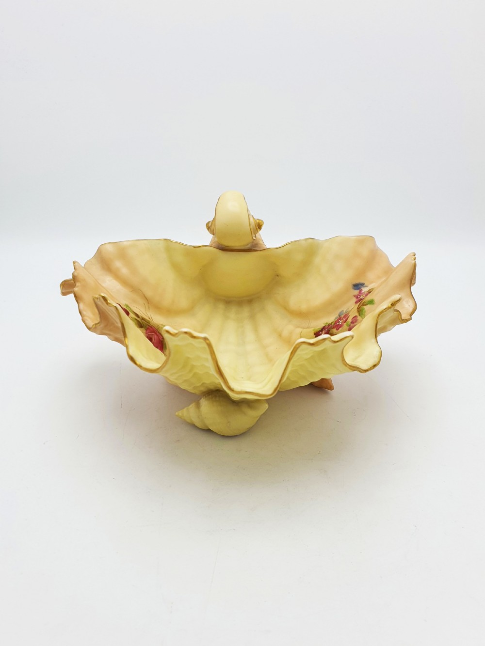 A shell-shaped antique blush ivory porcelain dish featuring soft peach shading, hand-painted pink floral sprays, textured ridges, and a gilded scalloped edge. View VII