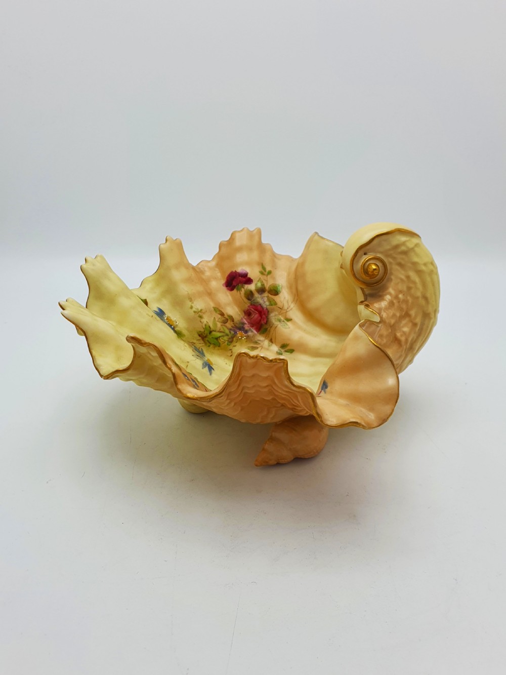 A shell-shaped antique blush ivory porcelain dish featuring soft peach shading, hand-painted pink floral sprays, textured ridges, and a gilded scalloped edge. View VIII