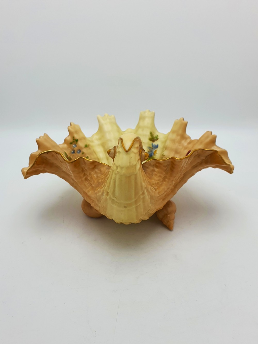 A shell-shaped antique blush ivory porcelain dish featuring soft peach shading, hand-painted pink floral sprays, textured ridges, and a gilded scalloped edge. View IX