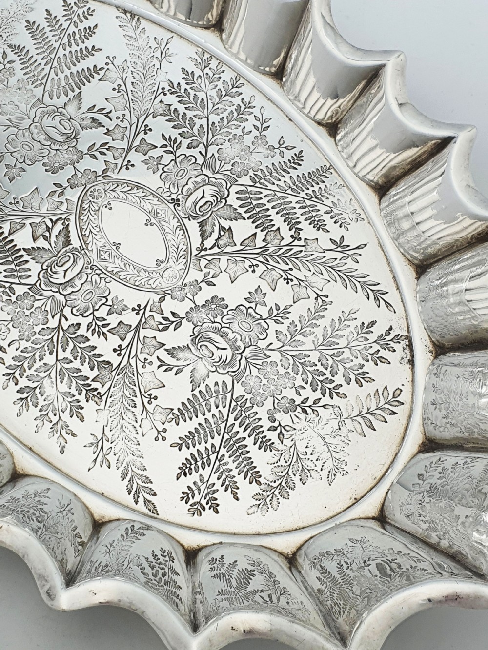 An oval silver plate serving dish featuring intricate floral engravings in the centre and a fluted scalloped outer rim. View IV