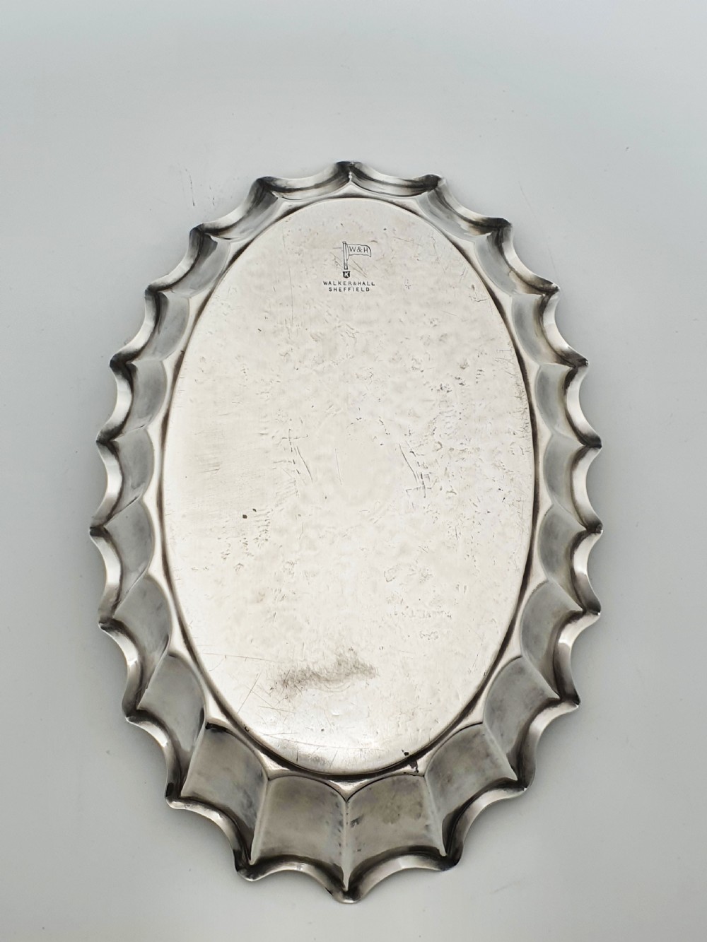 An oval silver plate serving dish featuring intricate floral engravings in the centre and a fluted scalloped outer rim. View V