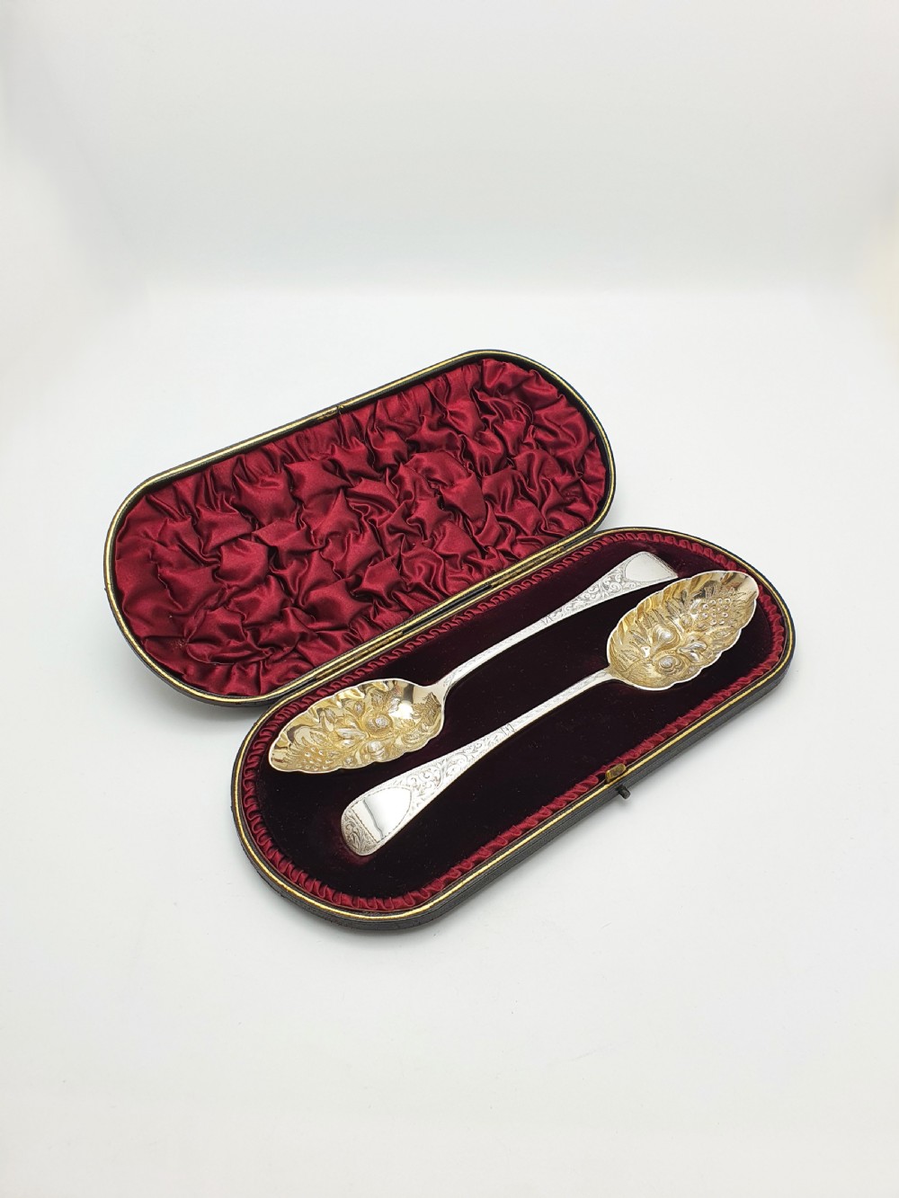 A pair of Victorian sterling silver berry spoons with embossed gilt fruit bowls and engraved handles, presented in a fitted velvet-lined case.