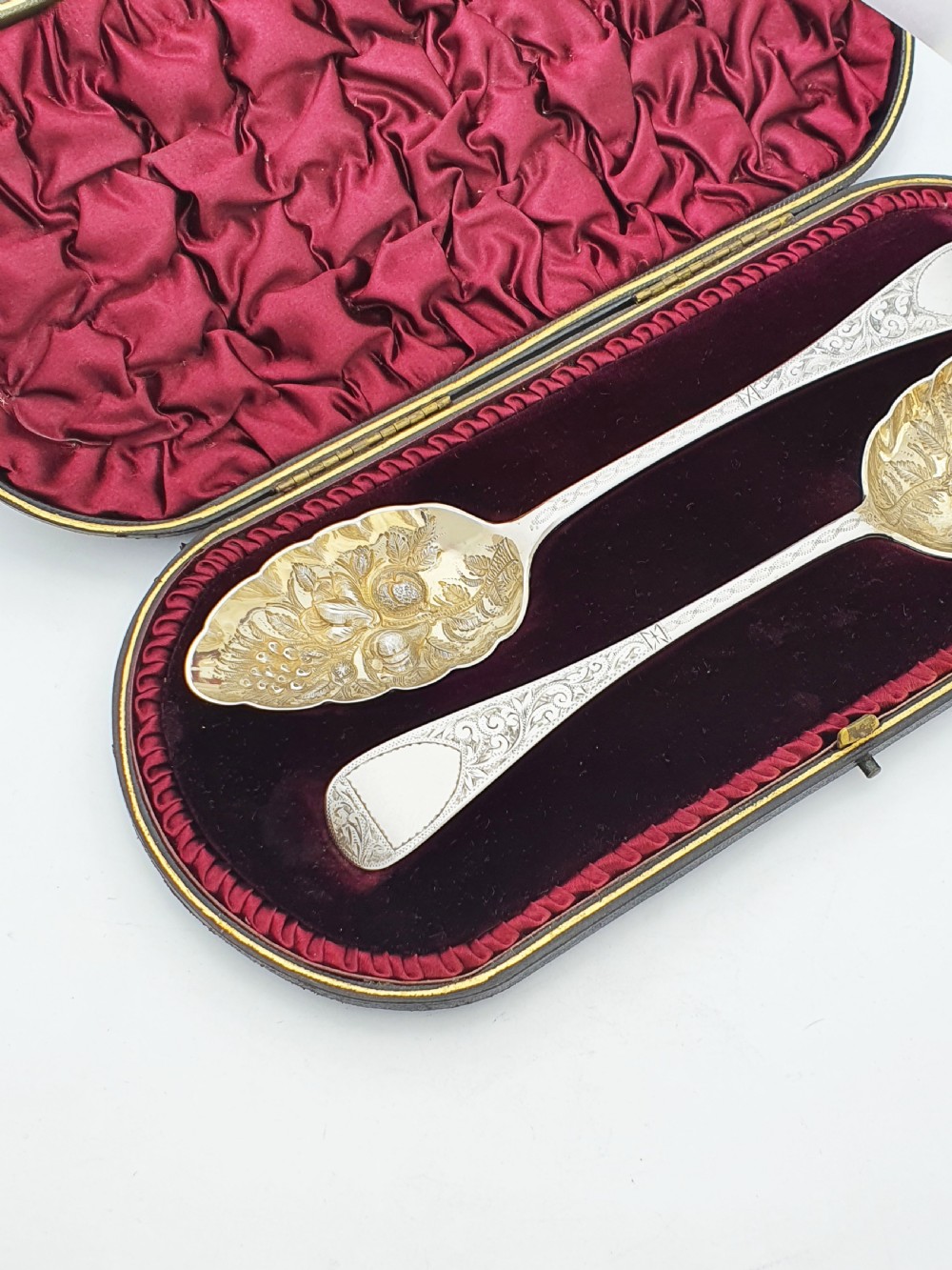 A pair of Victorian sterling silver berry spoons with embossed gilt fruit bowls and engraved handles, presented in a fitted velvet-lined case. View II