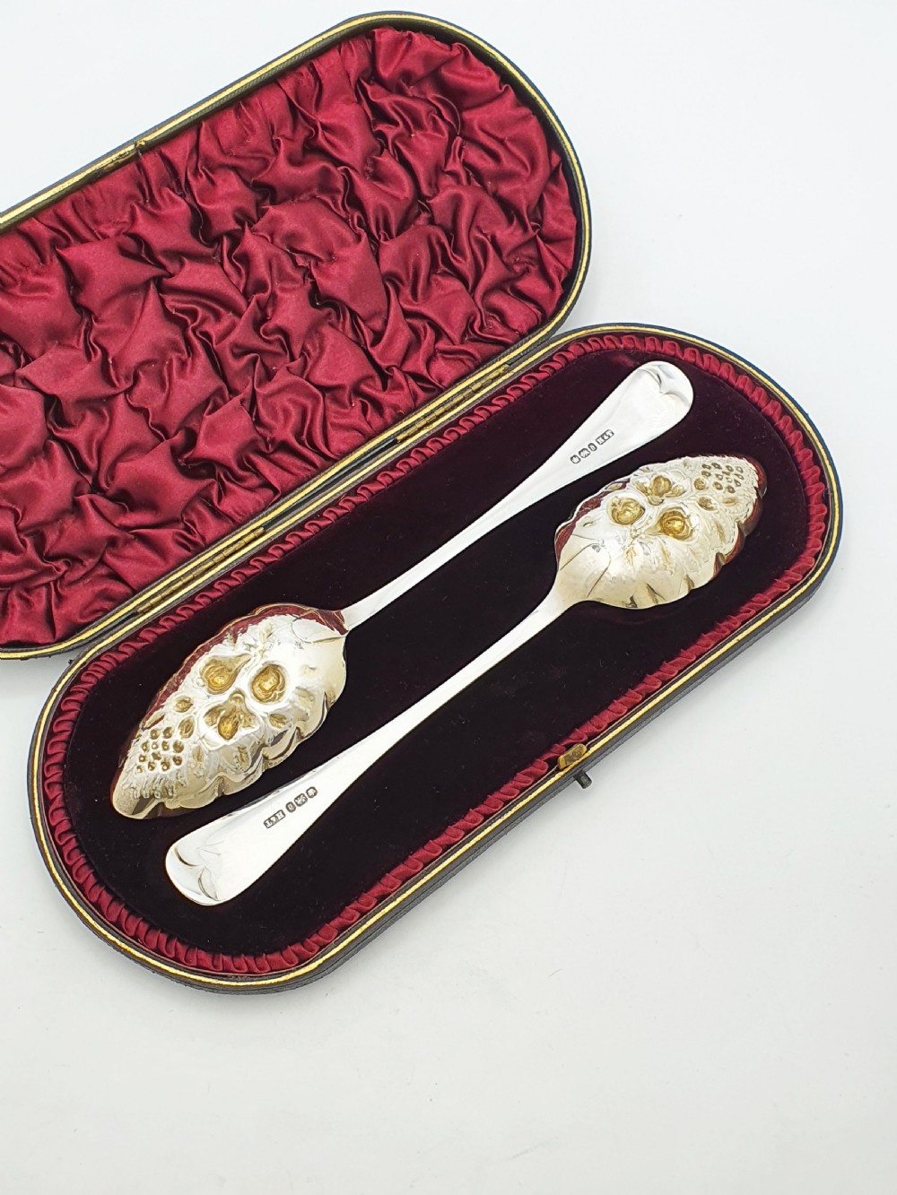 A pair of Victorian sterling silver berry spoons with embossed gilt fruit bowls and engraved handles, presented in a fitted velvet-lined case. View V