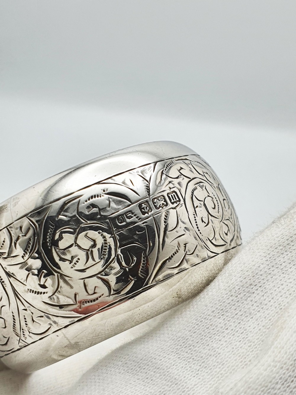 A pair of engraved sterling silver napkin rings with circular cartouches resting inside a dark blue velvet-lined presentation box. View IV