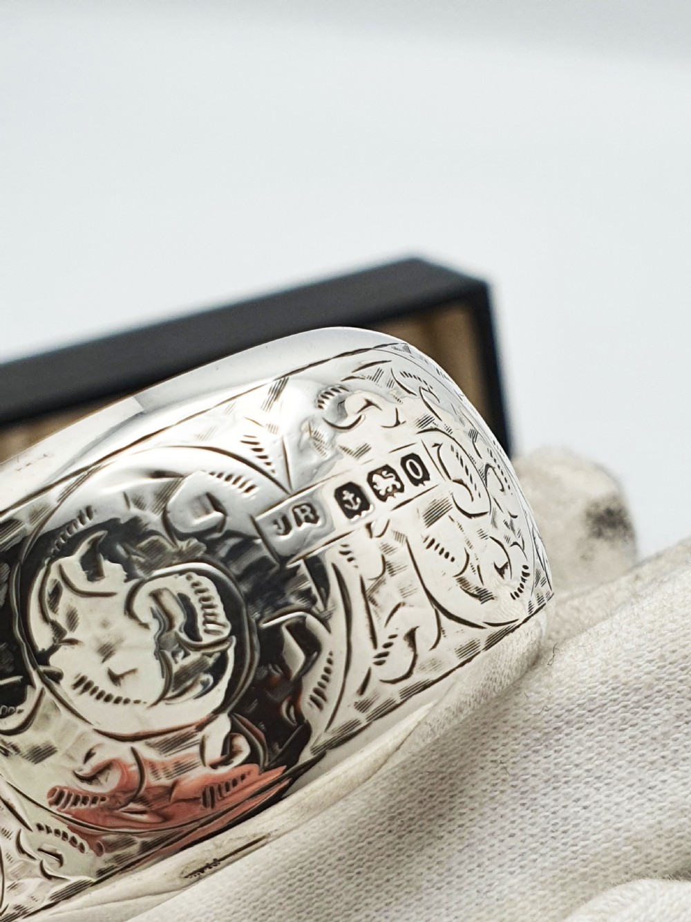 A pair of engraved sterling silver napkin rings with circular cartouches resting inside a dark blue velvet-lined presentation box. View V