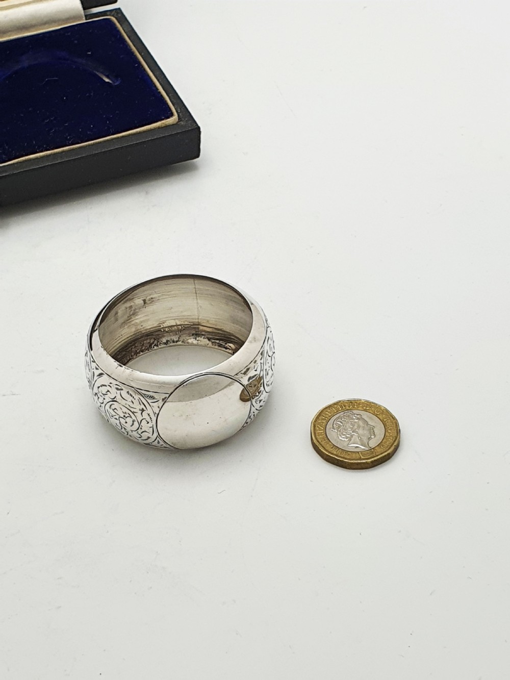 A pair of engraved sterling silver napkin rings with circular cartouches resting inside a dark blue velvet-lined presentation box. View VIII