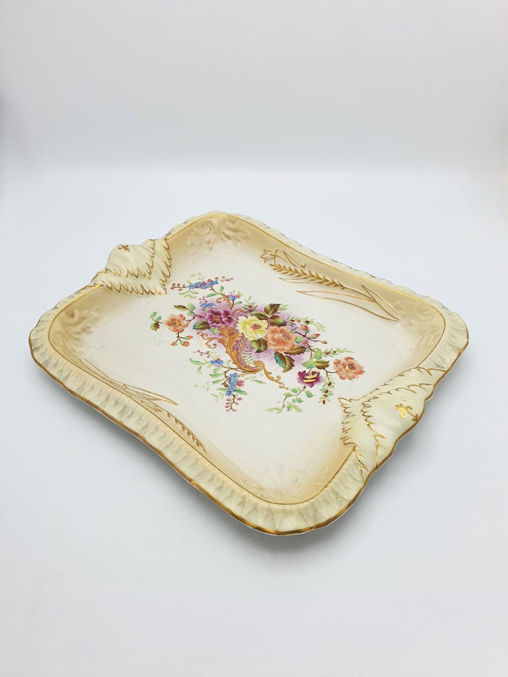 A rectangular cream ceramic tray with a central floral motif and gilded relief border.
