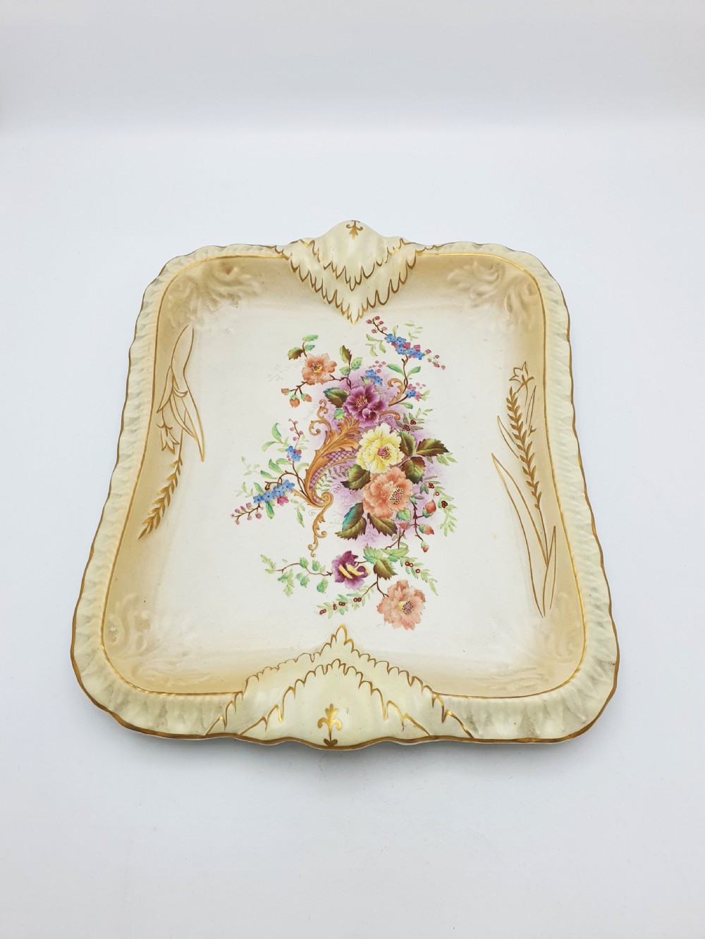 A rectangular cream ceramic tray with a central floral motif and gilded relief border. View III