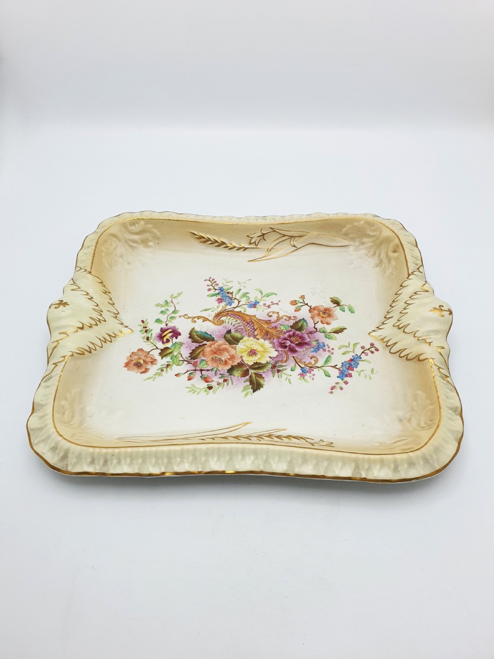 A rectangular cream ceramic tray with a central floral motif and gilded relief border. View IV