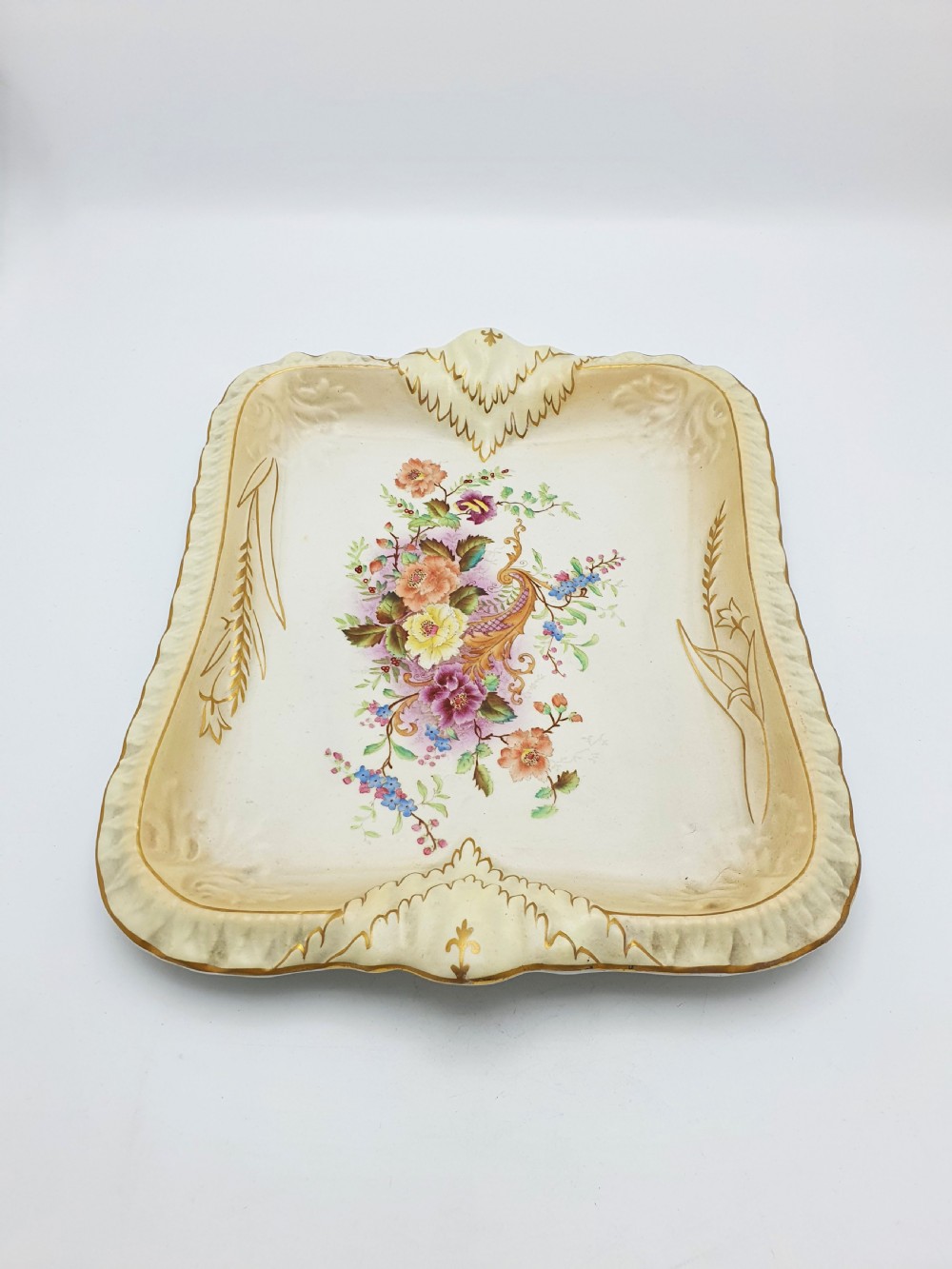 A rectangular cream ceramic tray with a central floral motif and gilded relief border. View V