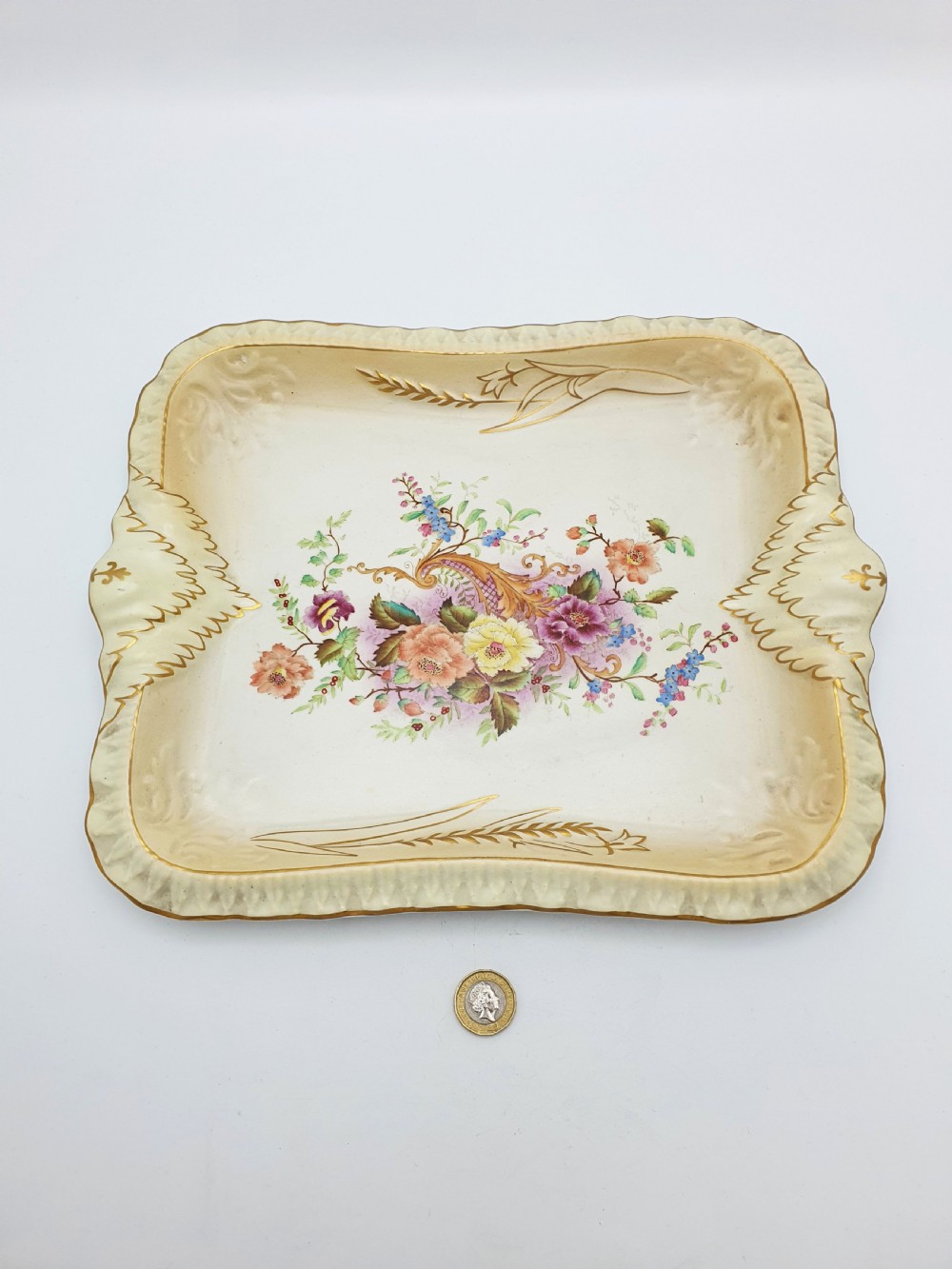 A rectangular cream ceramic tray with a central floral motif and gilded relief border. View IX