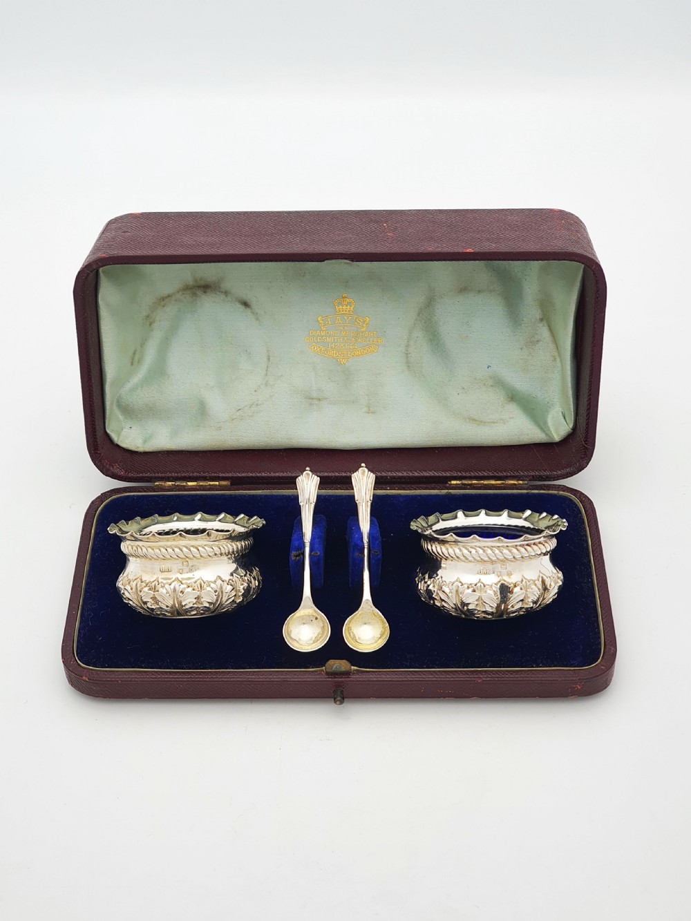 A pair of Victorian sterling silver open salt cellars with repousse leaf decoration and matching silver spoons in a velvet-lined maroon fitted box.