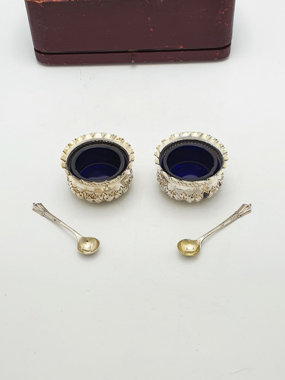 A pair of Victorian sterling silver open salt cellars with repousse leaf decoration and matching silver spoons in a velvet-lined maroon fitted box. View IV