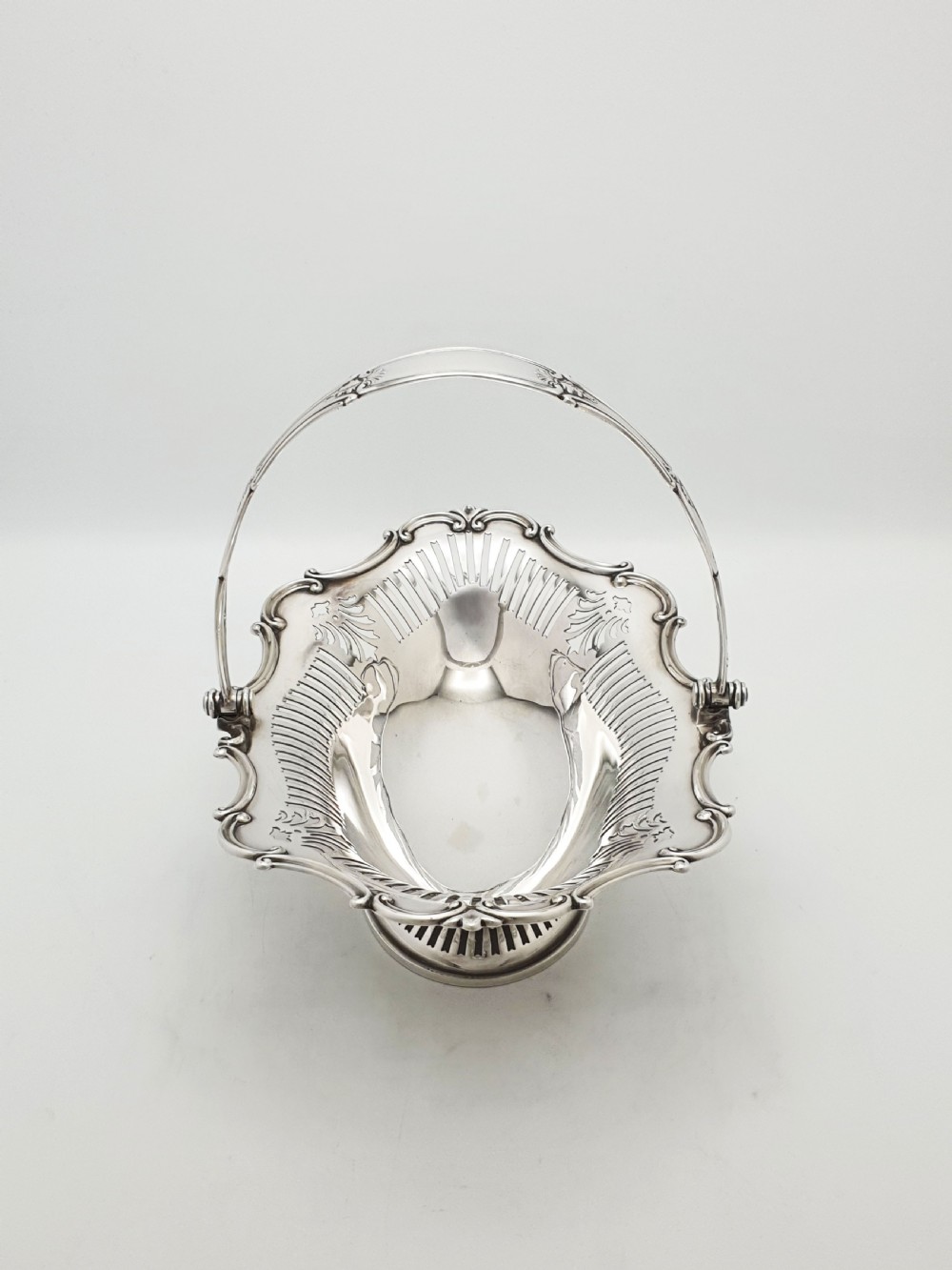 A George V silver-plated oval basket featuring a pierced border, relief rococo scroll edging, and a central hinged swing handle. View II
