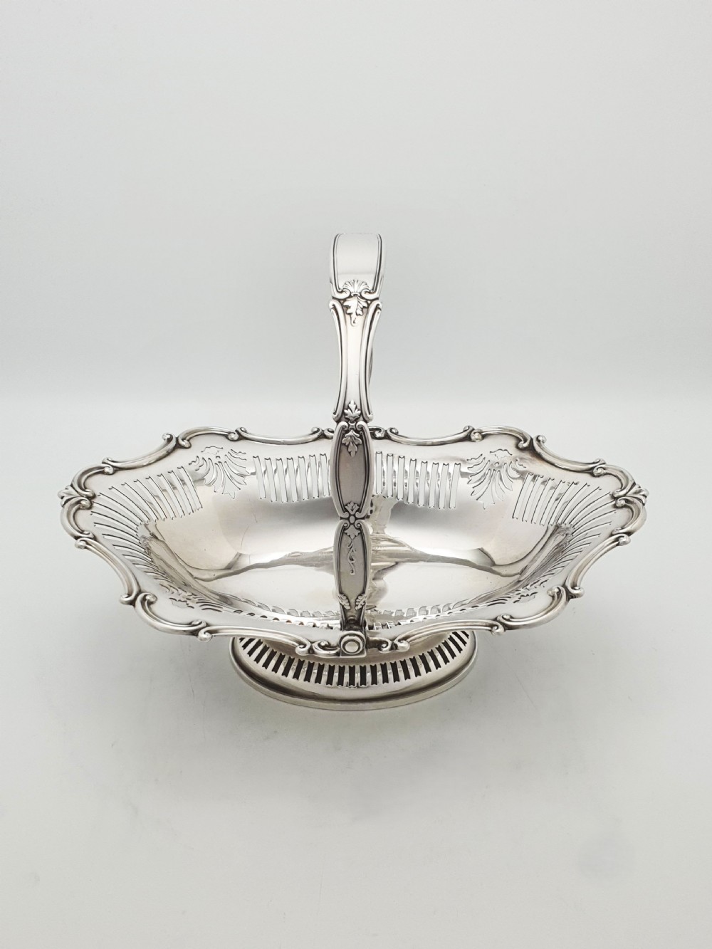 A George V silver-plated oval basket featuring a pierced border, relief rococo scroll edging, and a central hinged swing handle. View III