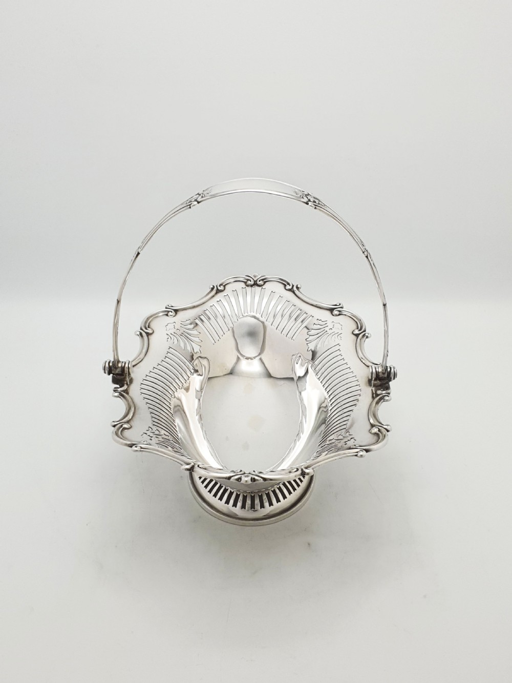 A George V silver-plated oval basket featuring a pierced border, relief rococo scroll edging, and a central hinged swing handle. View IV