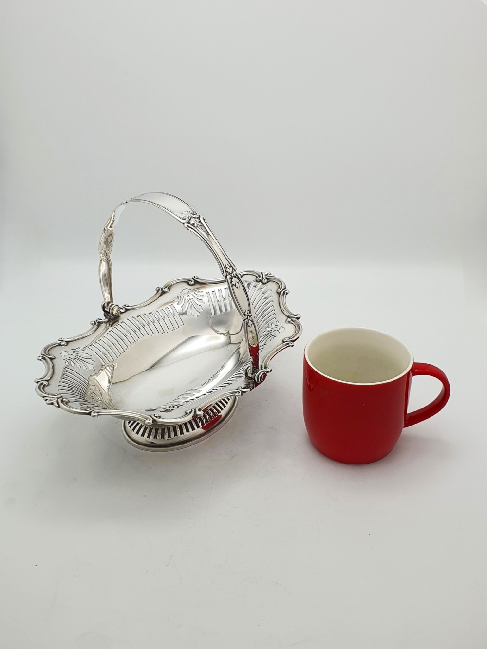 A George V silver-plated oval basket featuring a pierced border, relief rococo scroll edging, and a central hinged swing handle. View VIII