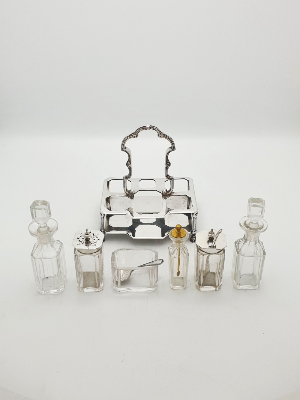 A Victorian silver-plated bachelor cruet set featuring an ornate handle frame holding multiple cut-glass condiment bottles. View VI