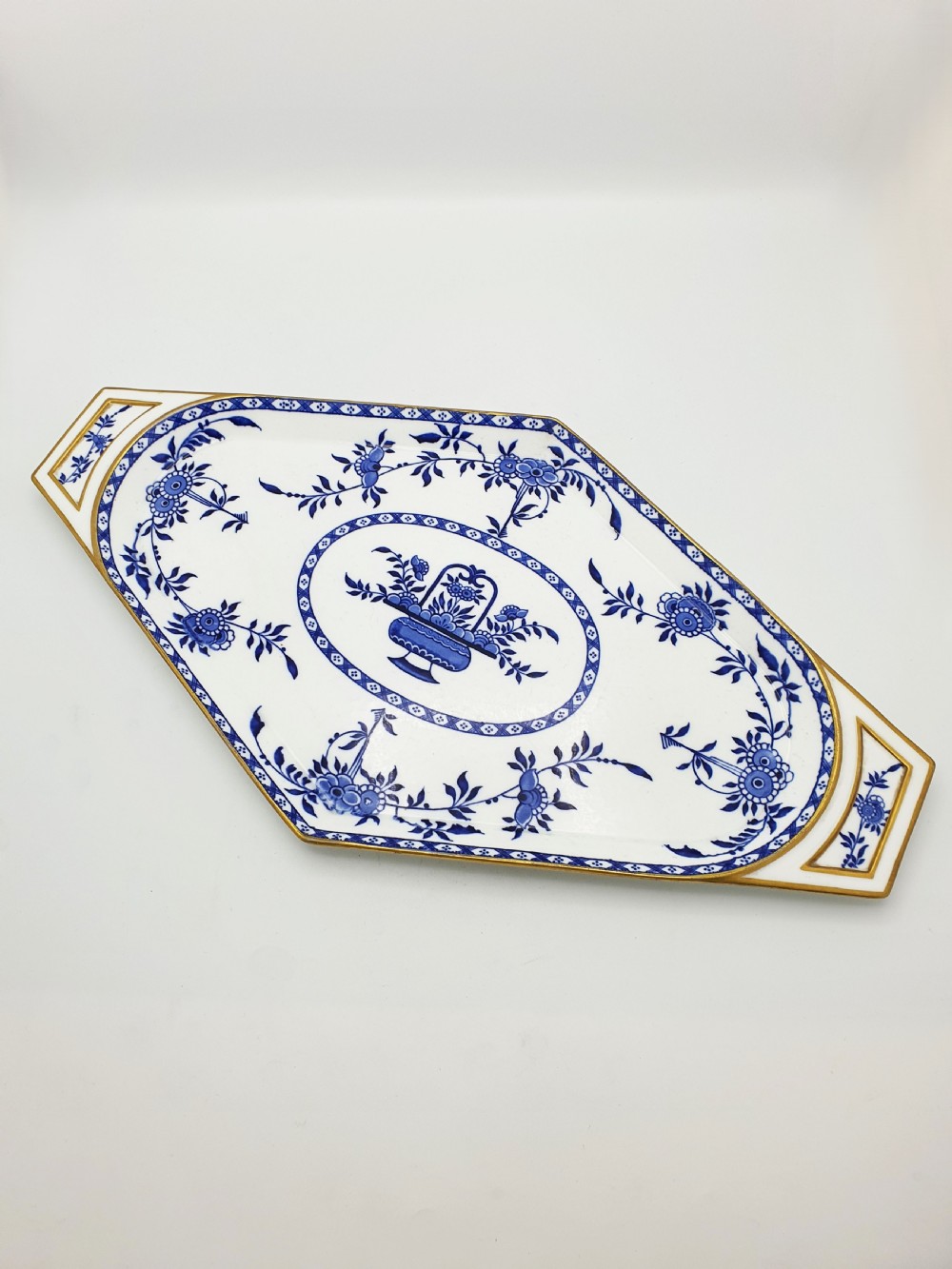An elongated diamond-shaped white porcelain tray decorated with blue floral transfers, a central floral basket motif, and gilded handles. View III