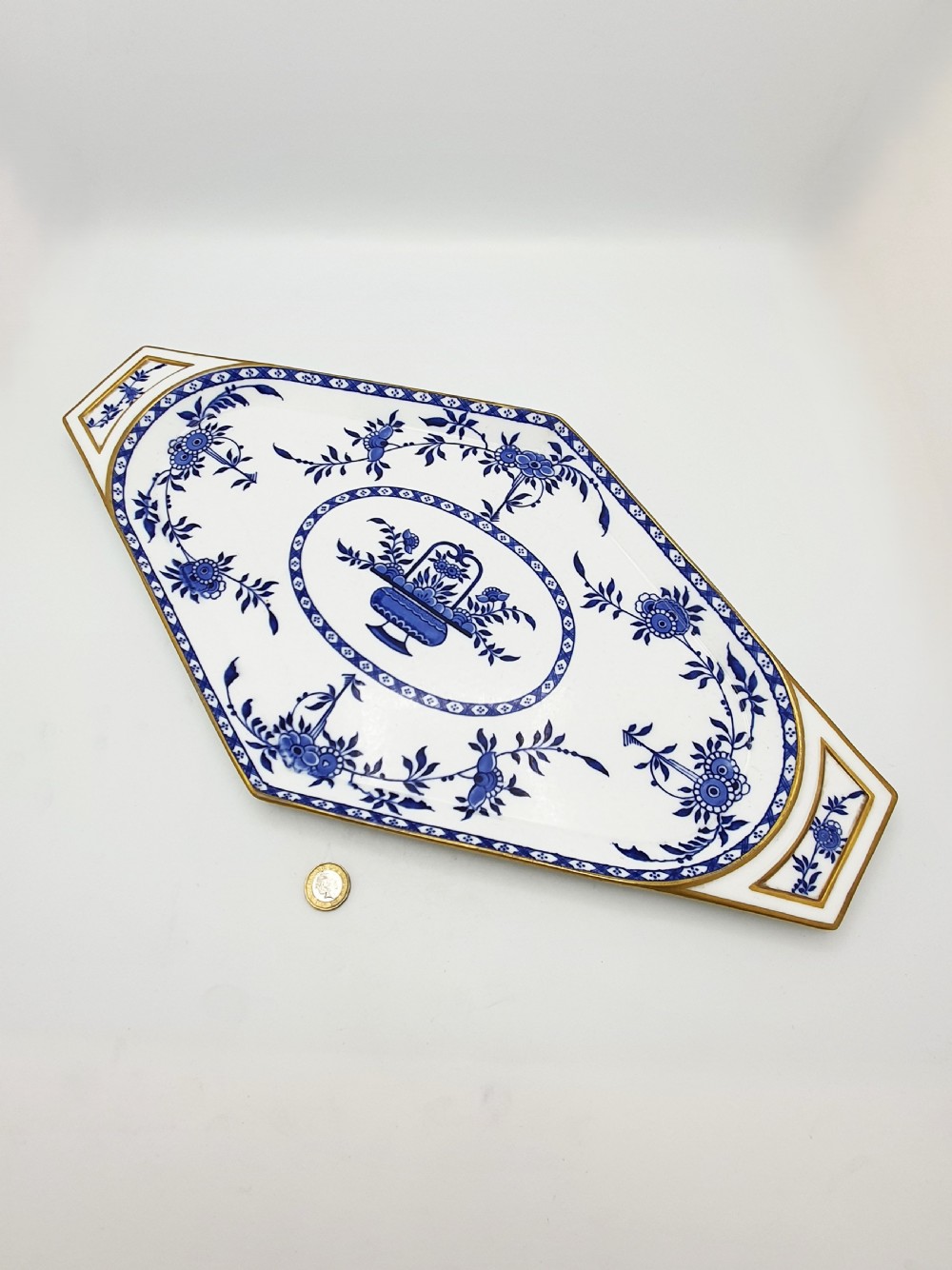 An elongated diamond-shaped white porcelain tray decorated with blue floral transfers, a central floral basket motif, and gilded handles. View VI