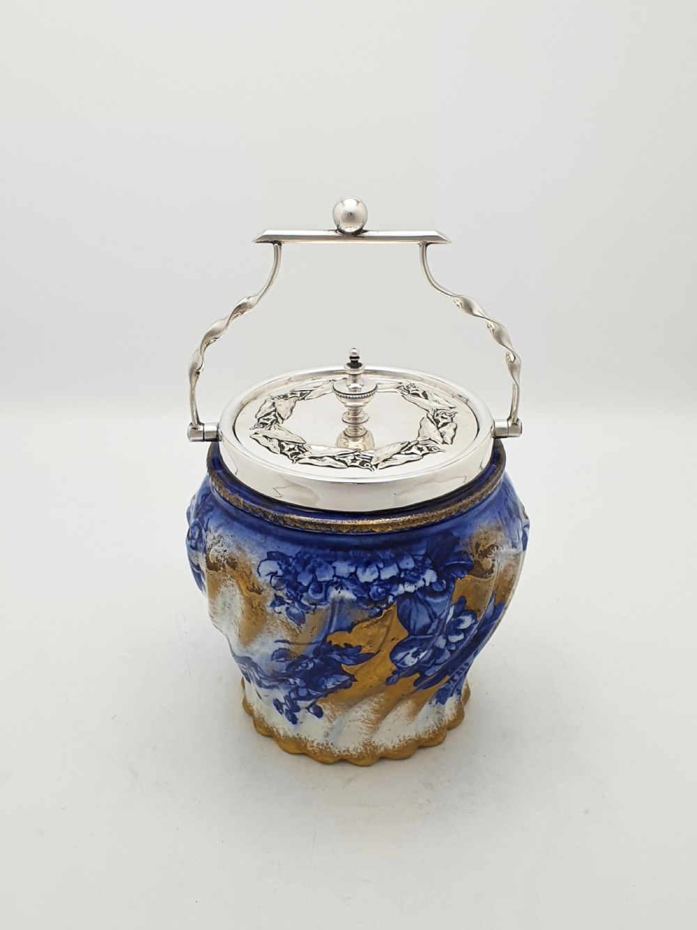 An Edwardian flow blue ceramic biscuit barrel featuring cobalt blue floral motifs, gilded accents, and a silver-plated lid with a twisted swing handle. View II