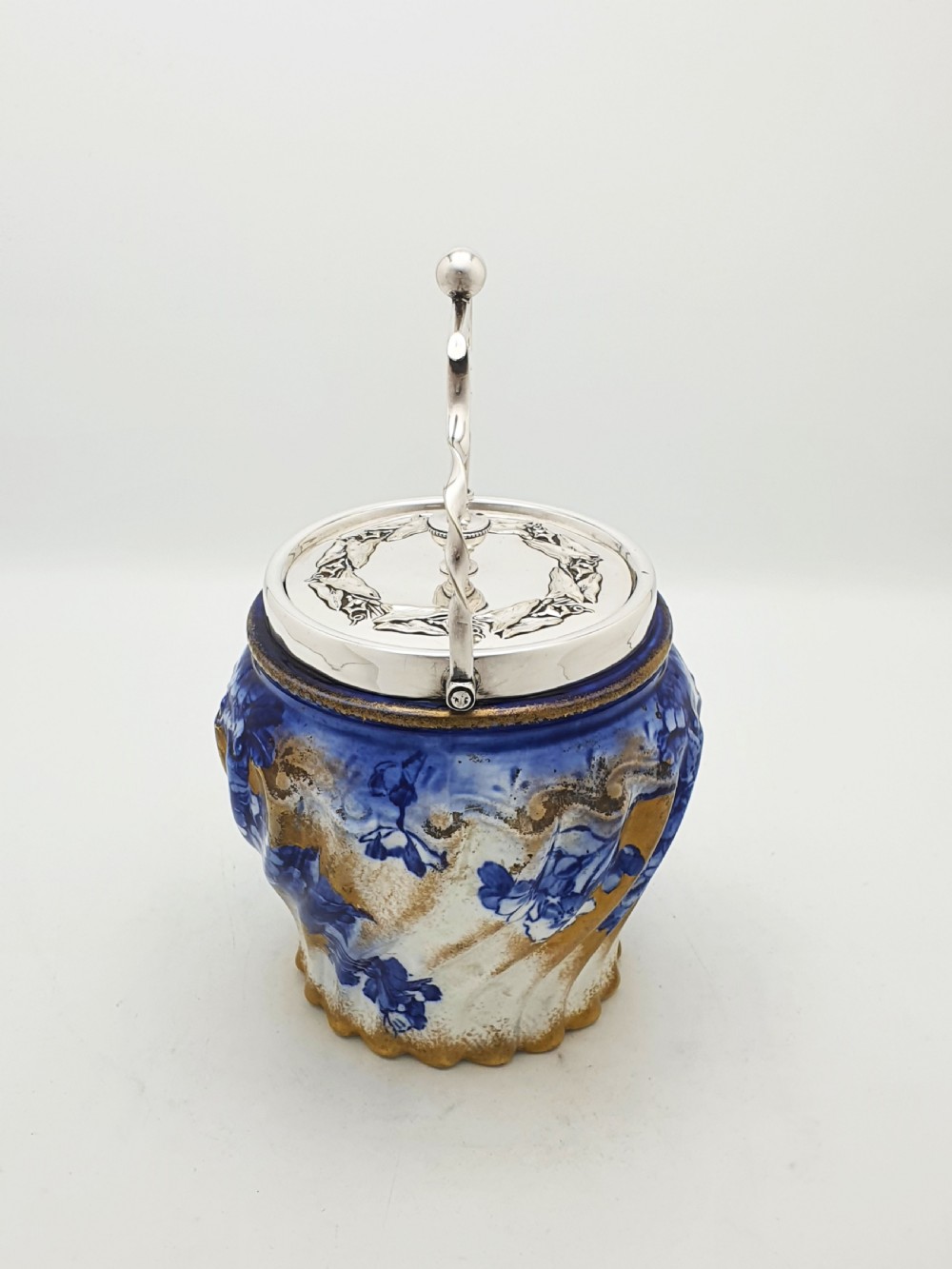 An Edwardian flow blue ceramic biscuit barrel featuring cobalt blue floral motifs, gilded accents, and a silver-plated lid with a twisted swing handle. View III