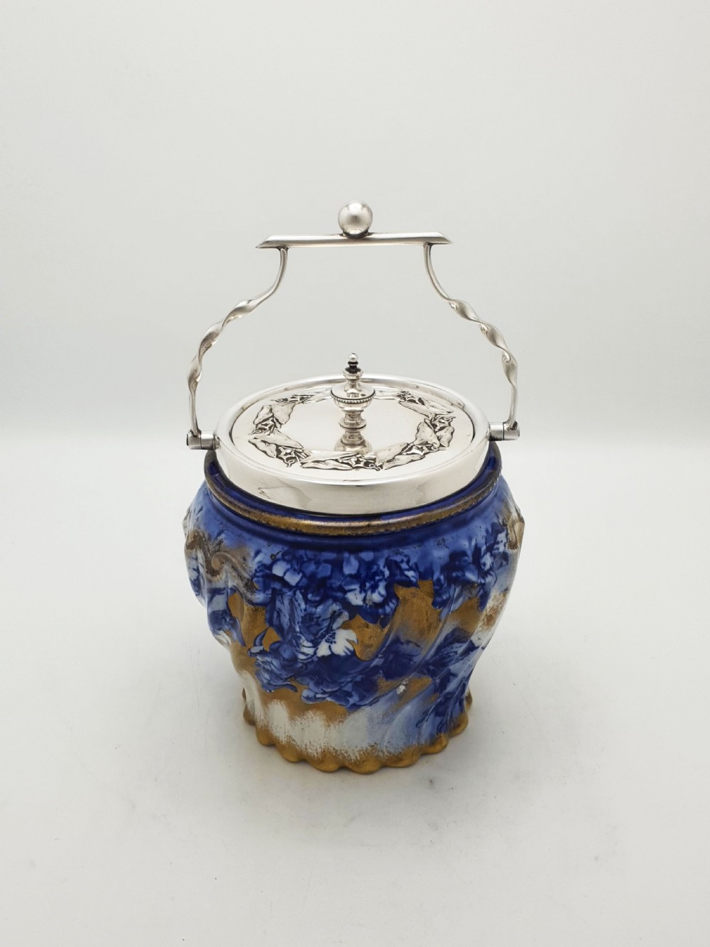 An Edwardian flow blue ceramic biscuit barrel featuring cobalt blue floral motifs, gilded accents, and a silver-plated lid with a twisted swing handle. View IV