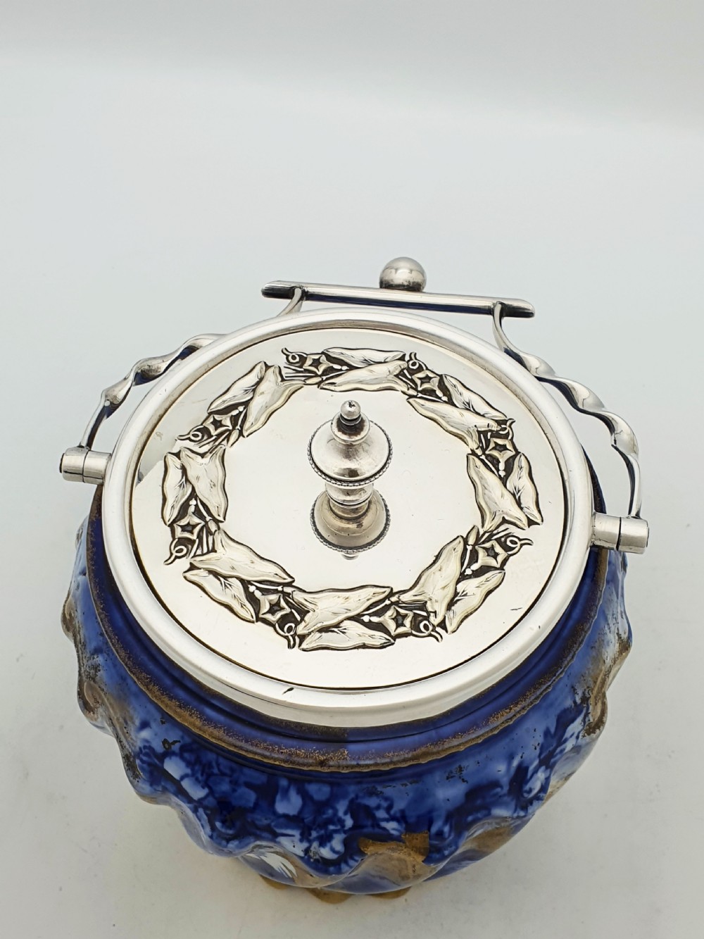 An Edwardian flow blue ceramic biscuit barrel featuring cobalt blue floral motifs, gilded accents, and a silver-plated lid with a twisted swing handle. View V