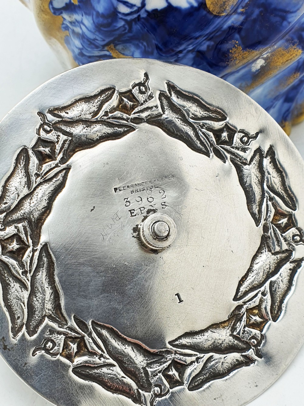 An Edwardian flow blue ceramic biscuit barrel featuring cobalt blue floral motifs, gilded accents, and a silver-plated lid with a twisted swing handle. View VI