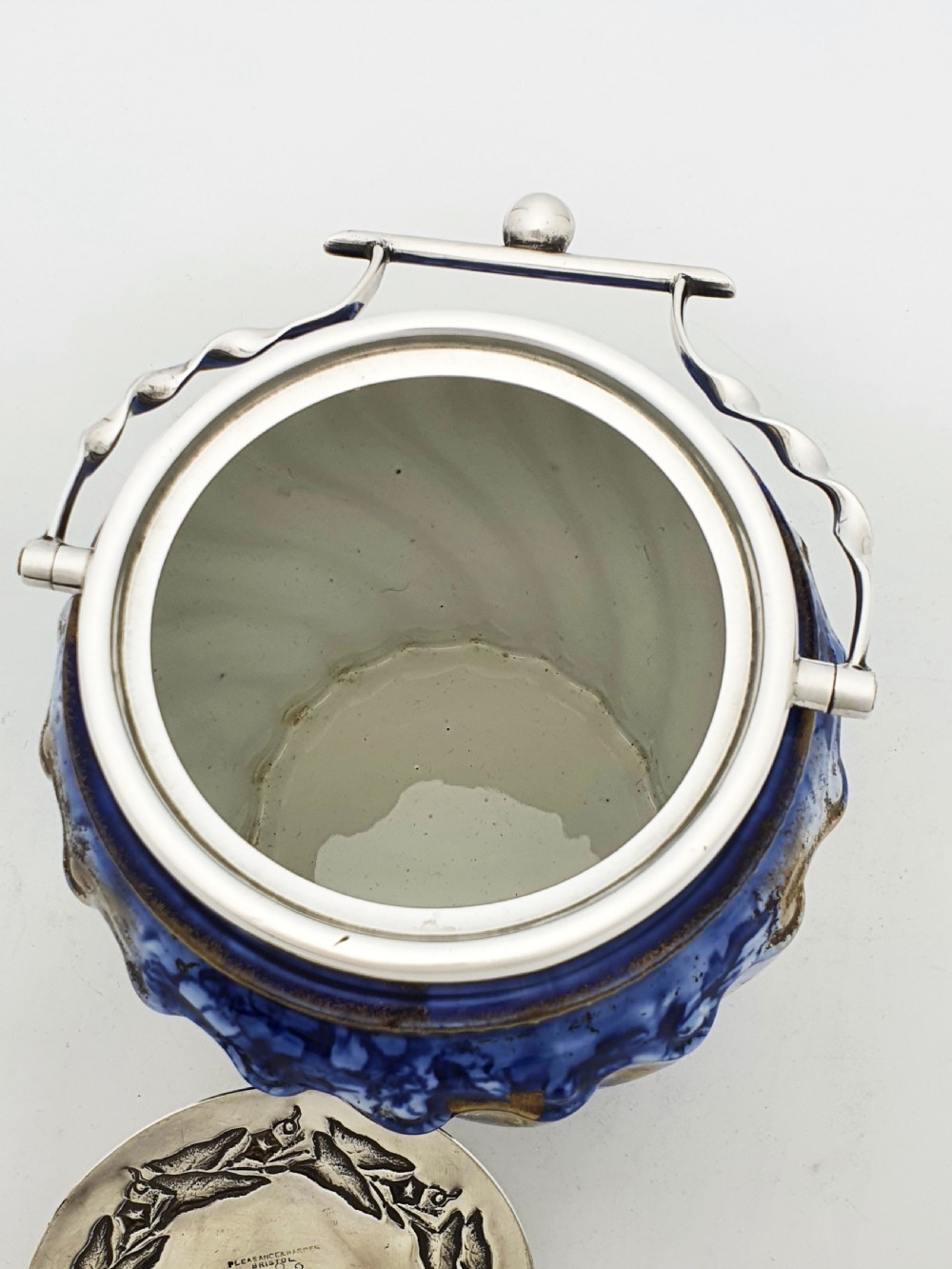 An Edwardian flow blue ceramic biscuit barrel featuring cobalt blue floral motifs, gilded accents, and a silver-plated lid with a twisted swing handle. View VII