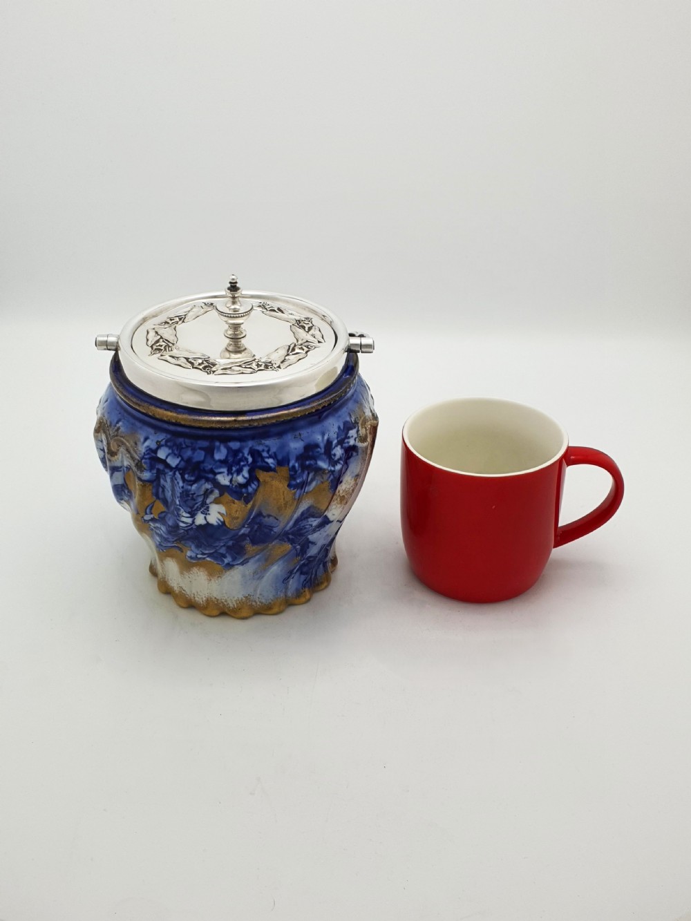 An Edwardian flow blue ceramic biscuit barrel featuring cobalt blue floral motifs, gilded accents, and a silver-plated lid with a twisted swing handle. View VIII