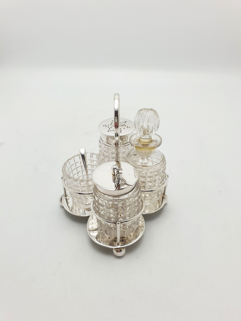 An antique silver-plated condiment caddy holding four faceted cut-glass bottles and pots with silver lids. View II