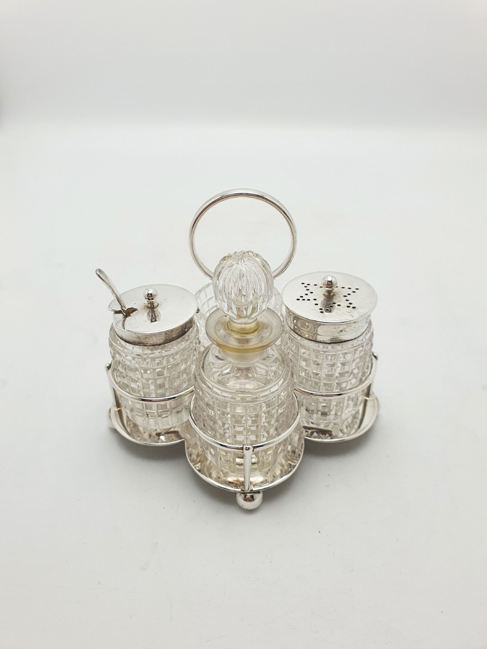 An antique silver-plated condiment caddy holding four faceted cut-glass bottles and pots with silver lids. View III
