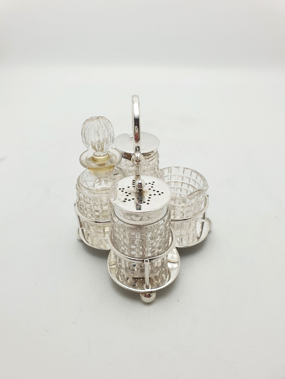An antique silver-plated condiment caddy holding four faceted cut-glass bottles and pots with silver lids. View IV