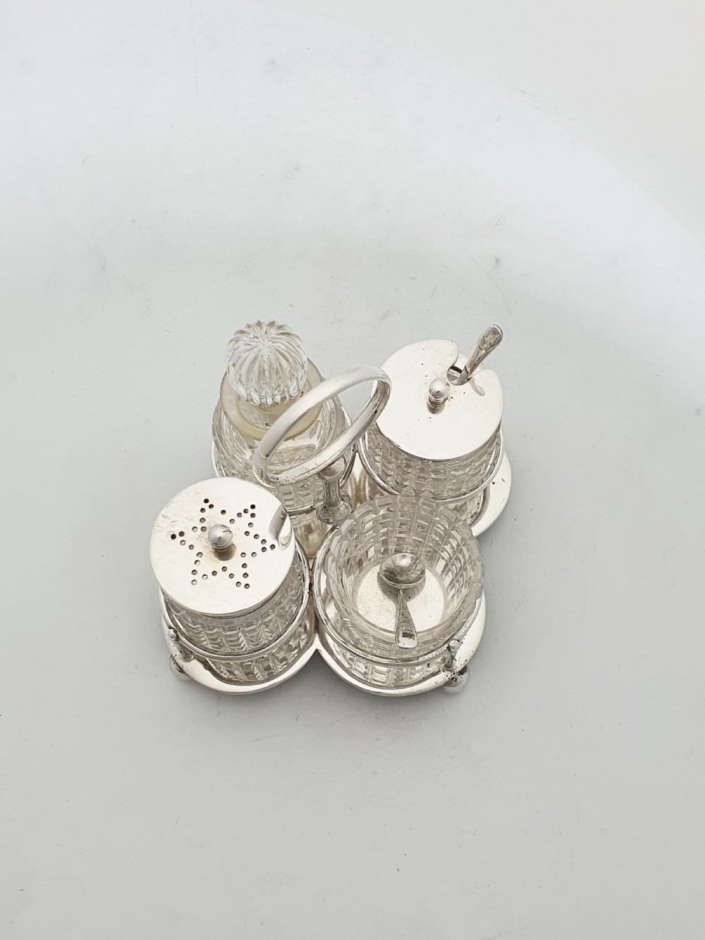 An antique silver-plated condiment caddy holding four faceted cut-glass bottles and pots with silver lids. View V