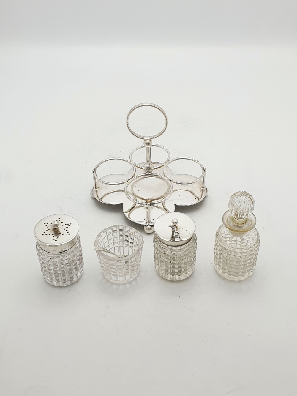 An antique silver-plated condiment caddy holding four faceted cut-glass bottles and pots with silver lids. View VI