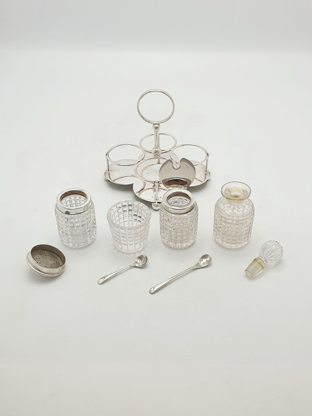 An antique silver-plated condiment caddy holding four faceted cut-glass bottles and pots with silver lids. View VII
