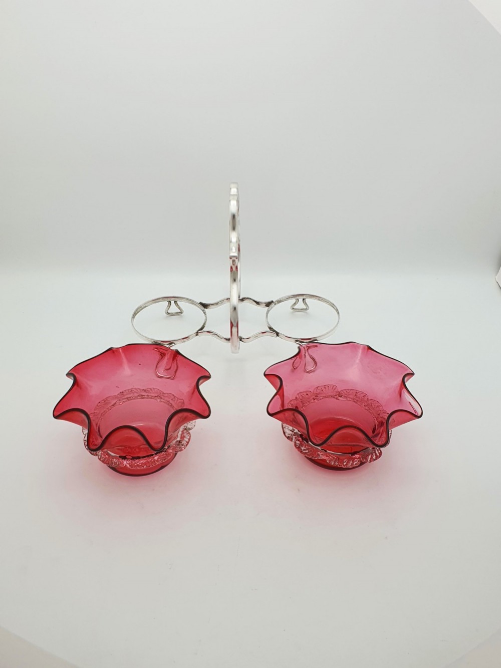 An Edwardian twin cranberry glass preserve dish set with crimped rims held in a silver-plated wireframe stand with a central handle. View III