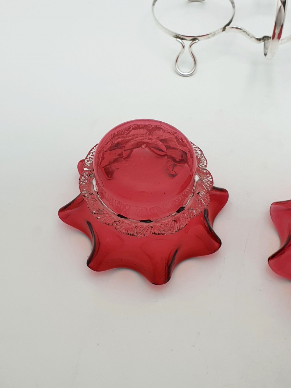 An Edwardian twin cranberry glass preserve dish set with crimped rims held in a silver-plated wireframe stand with a central handle. View IV