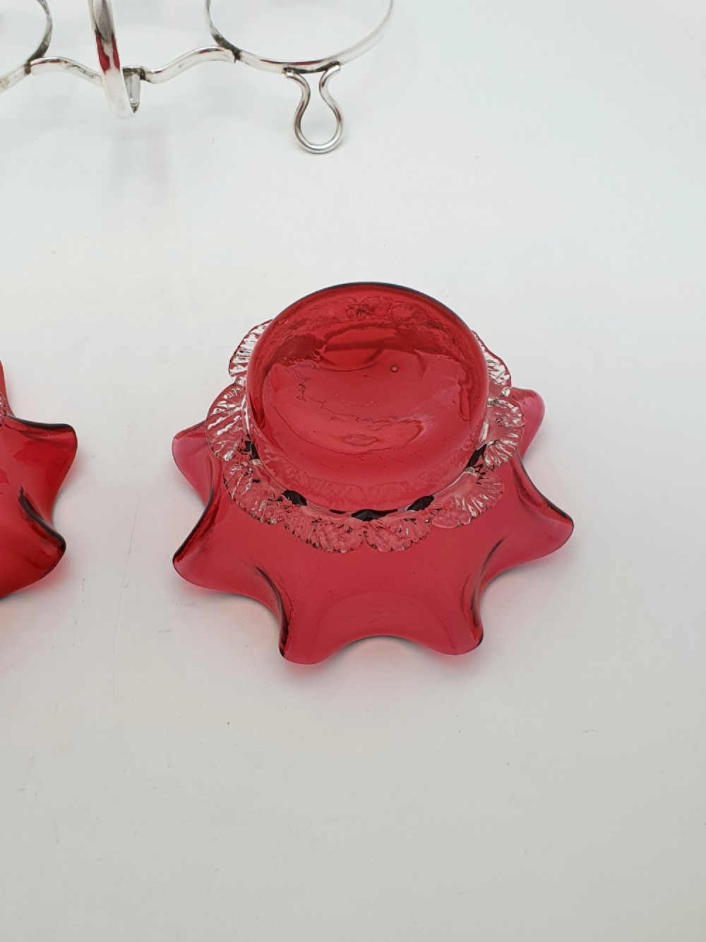 An Edwardian twin cranberry glass preserve dish set with crimped rims held in a silver-plated wireframe stand with a central handle. View V